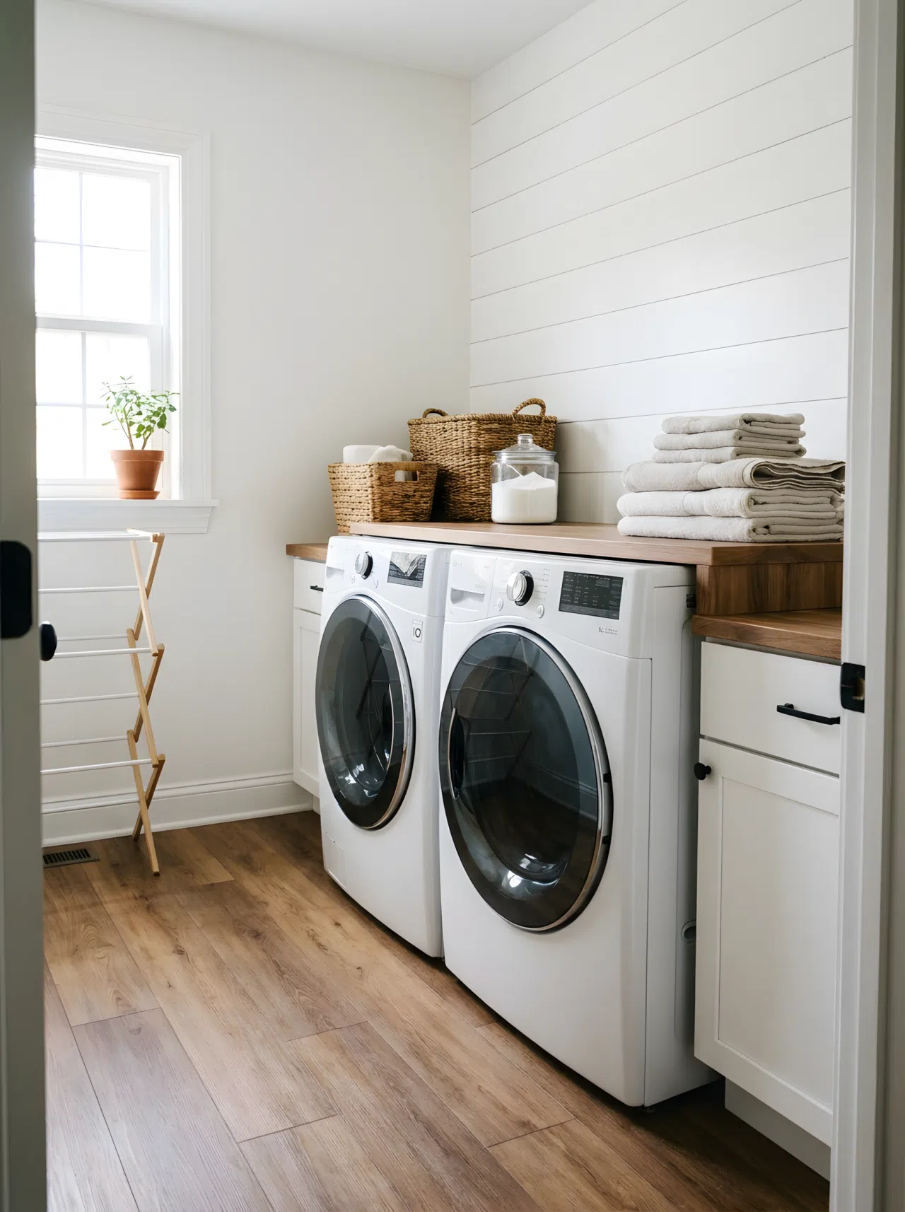 A small home laundry room with waterproof vinyl plank flooring in a warm wood tone, washer and dryer neatly arranged against a clean white wall, folded towels stacked beside them, bright natural light streaming through a nearby window, real-life photography style, organized and clean.