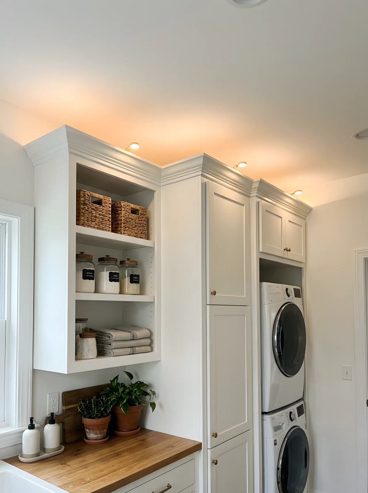 Real-life photography of small uplights placed on top of tall laundry cabinets, bouncing soft indirect light off the ceiling to fill the room evenly, shelves neatly made and beautifully arranged, organized clean space, realistic home photography.