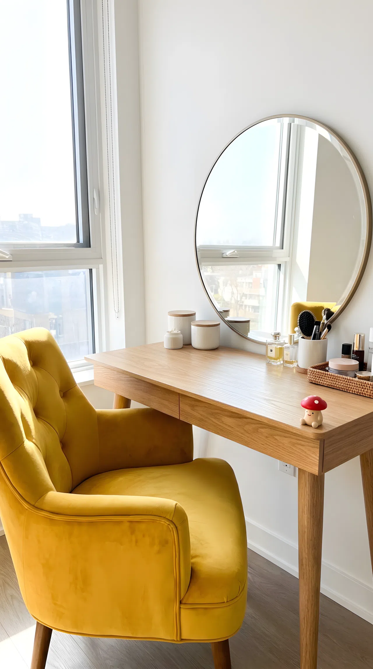Real-life photo of a bedroom vanity with a bold vibrant yellow velvet chair (RGB 244, 208, 63), neutral wood table, round mirror, neatly made surface, beautifully arranged makeup items, small red mushroom toy figurine on the table edge, bright natural light, clean and organized, vivid stock photography.