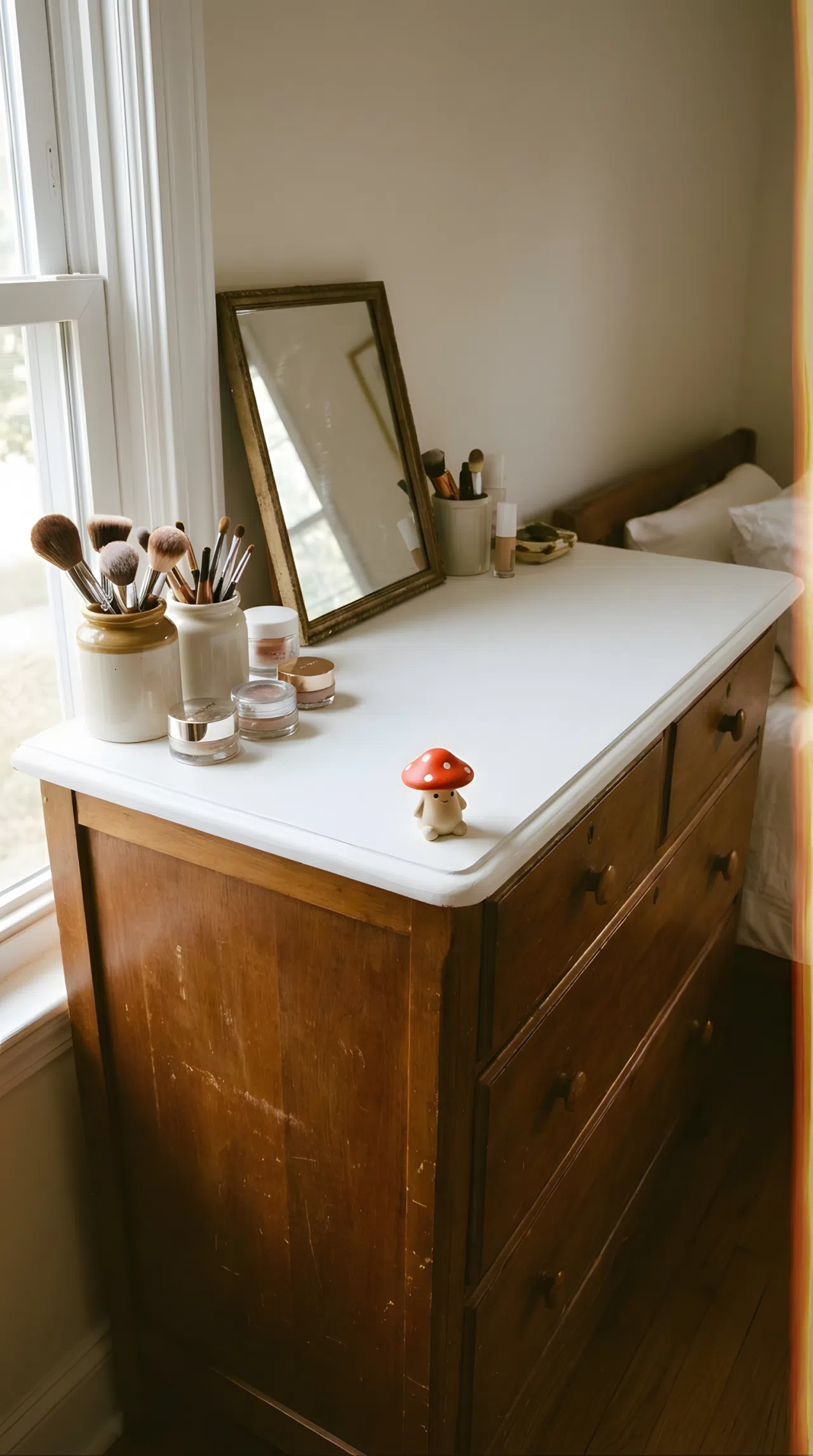 Real-life photo of a repurposed vintage dresser turned into a bedroom vanity, freshly painted white top, small mirror placed on top, neatly made surface, beautifully arranged makeup brushes, small red mushroom toy figurine on the dresser edge, bright natural light, clean and organized, vibrant stock photography.