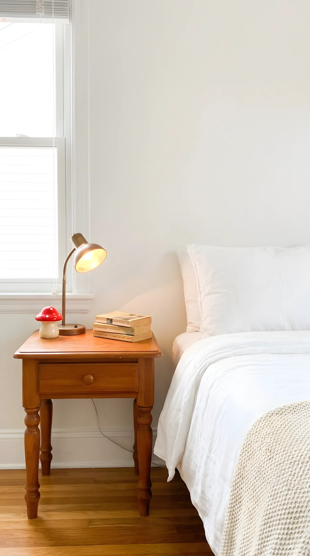 Real-life photograph, stock photo style, thrifted wooden nightstand beside neatly made bed, small lamp, stack of books, small cute red mushroom-shaped toy beside lamp, beautifully arranged, clean and organized, bright natural light, vibrant warm wood tones, Pinterest-ready, not a render, not an illustration.