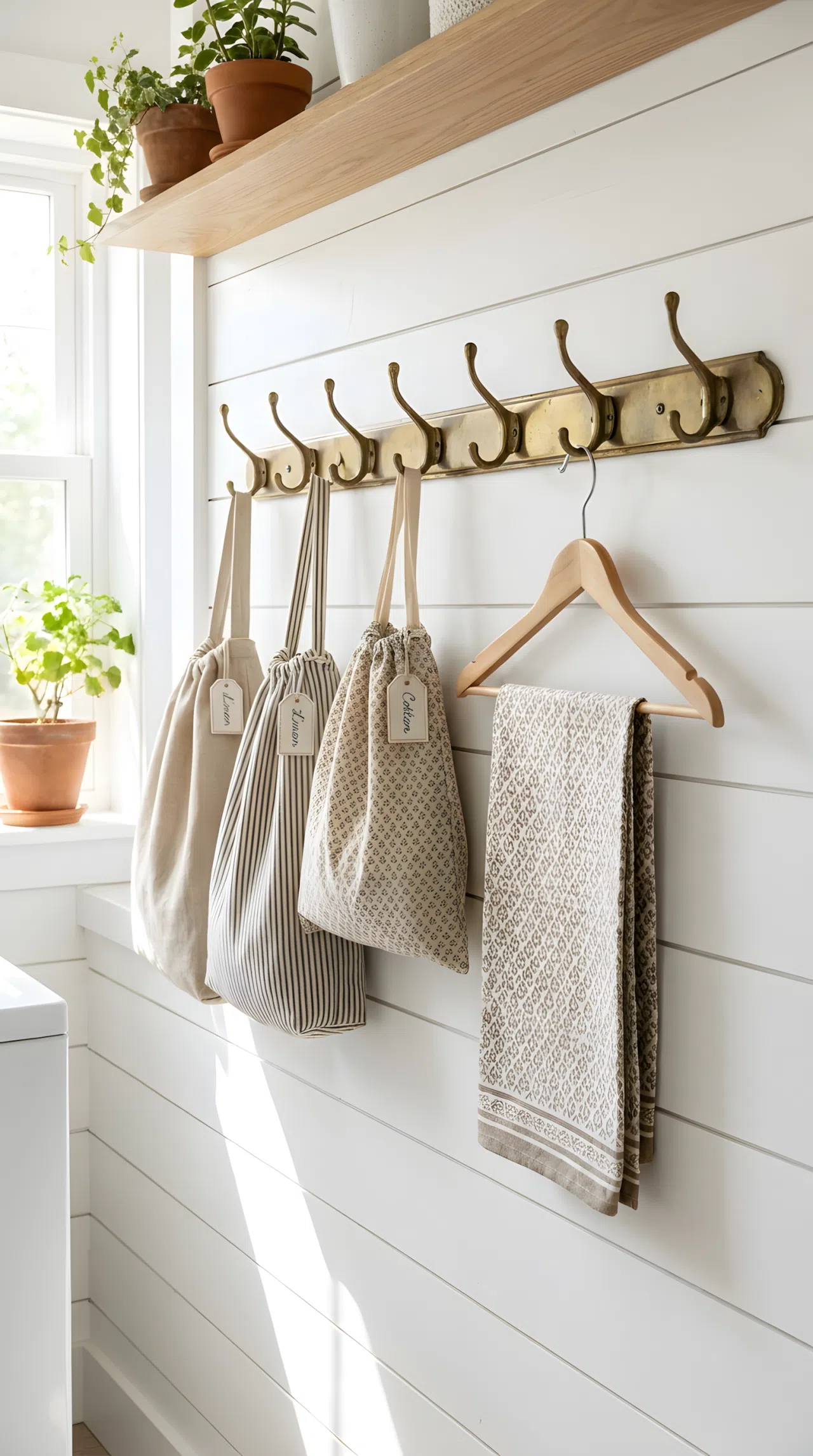 A real-life laundry room wall with a brass hook rail holding neatly hung linen bags and a drying cloth, beautifully arranged, clean and organized, bright natural light, vibrant stock photography style, no text overlays, no people