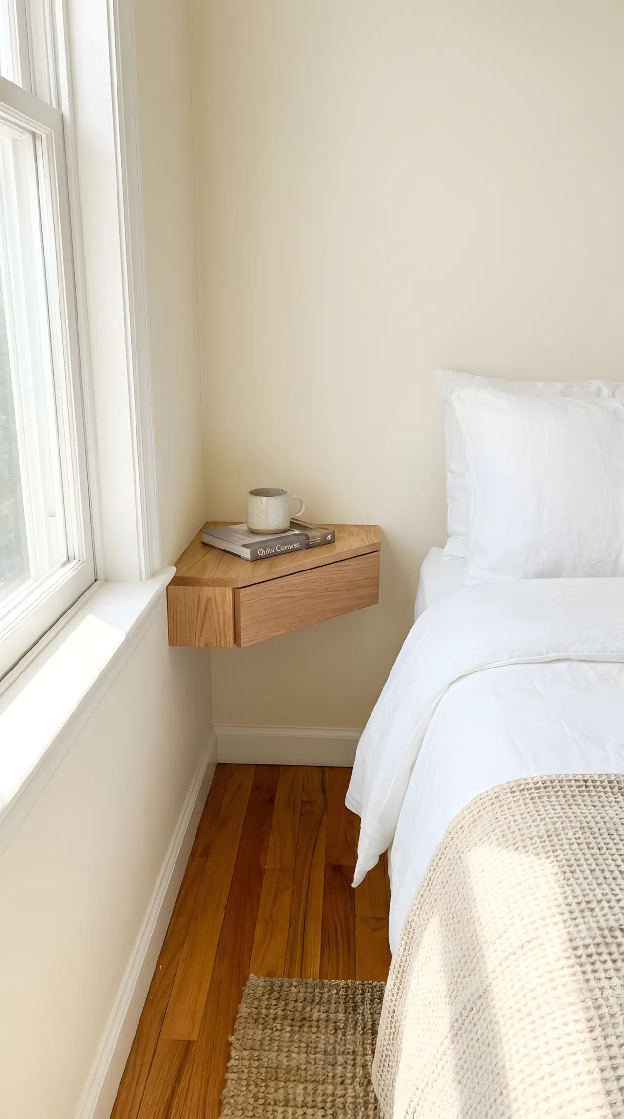 Stock photography, real-life practical compact small bedroom corner, a sleek floating oak corner nightstand mounted flush in a tight wall corner next to a bed fitted snugly in the room, a neatly made bed with white linen sheets, beautifully arranged ceramic cup and book on the nightstand shelf, clean hardwood floor underneath, organized small space, bright natural light pouring in from nearby window.