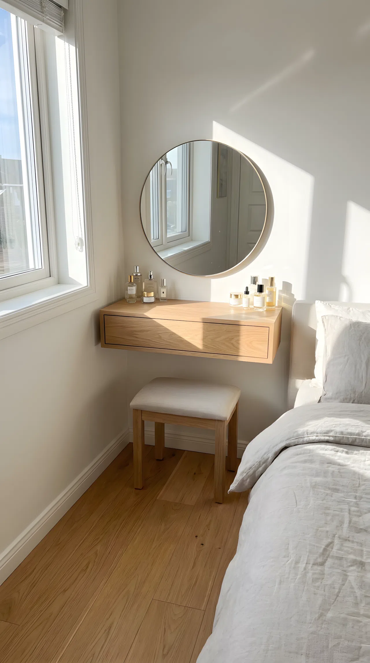 Bright real-life stock photography of a compact bedroom with a floating wooden vanity table mounted on the wall. Neatly arranged cosmetic bottles and a clean round mirror above it. Organized setup, clean floor, bright natural light pouring through nearby window, vibrant natural wood tones, practical small bedroom design.