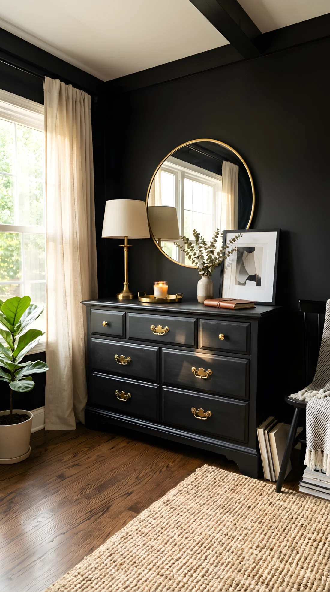 Wide-angle real photo of a black dresser with brass drawer pulls and knobs, matching brass table lamp base on top, black walls, bright natural light catching the brass hardware and creating warm highlights, neatly organized dresser top, dramatic wide camera angle showing the dresser and part of the room, photographic stock photo style, vibrant warm brass tones against black