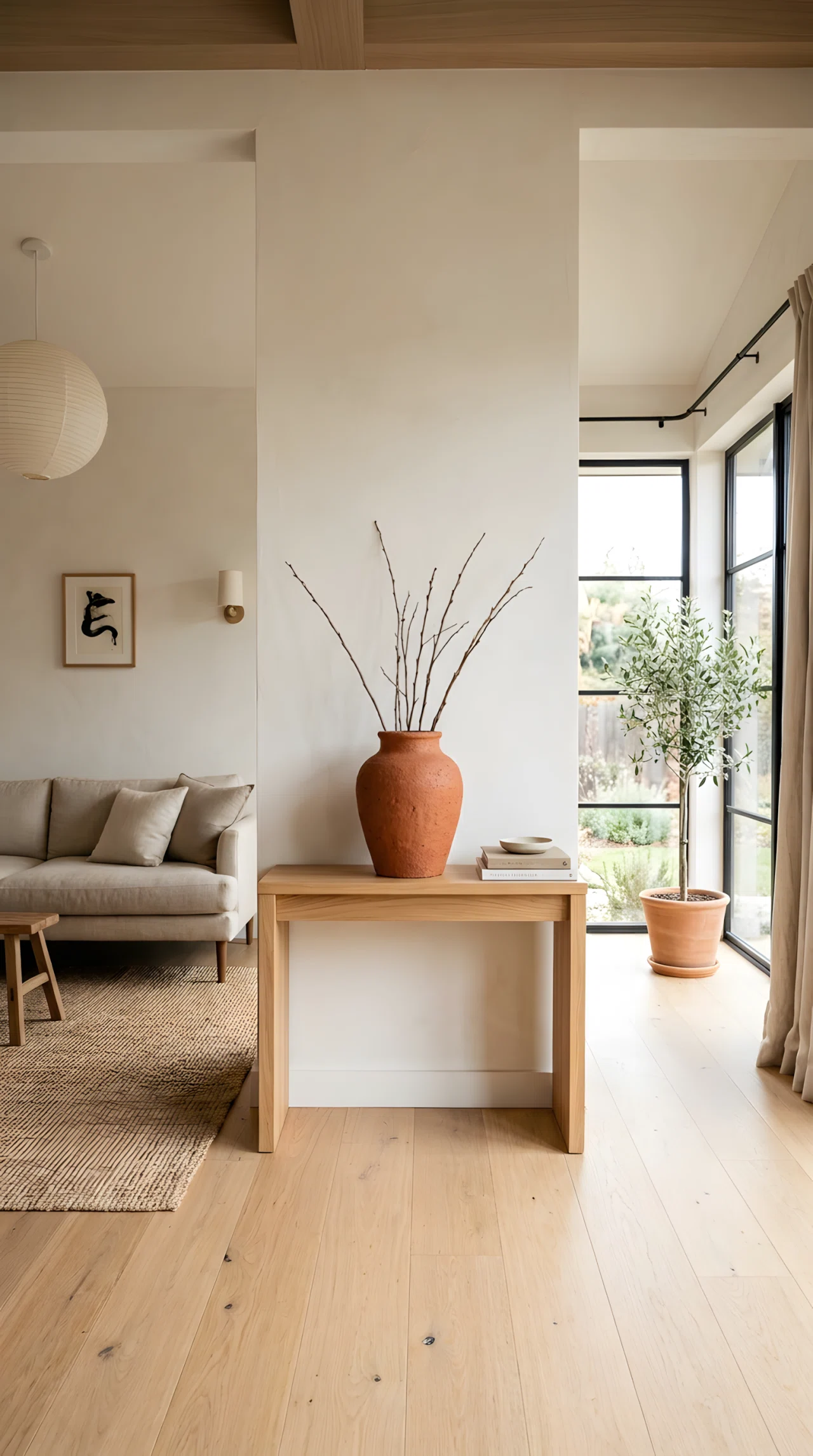 Wide-angle real-life photograph of a Japandi living room, a single handmade terracotta ceramic vase (RGB 196, 93, 60) placed on a light oak console table against a warm white wall, soft natural side lighting highlighting its texture, minimal surrounding furniture, dramatic wide camera angle, vibrant warm tones, stock photography style, no people.